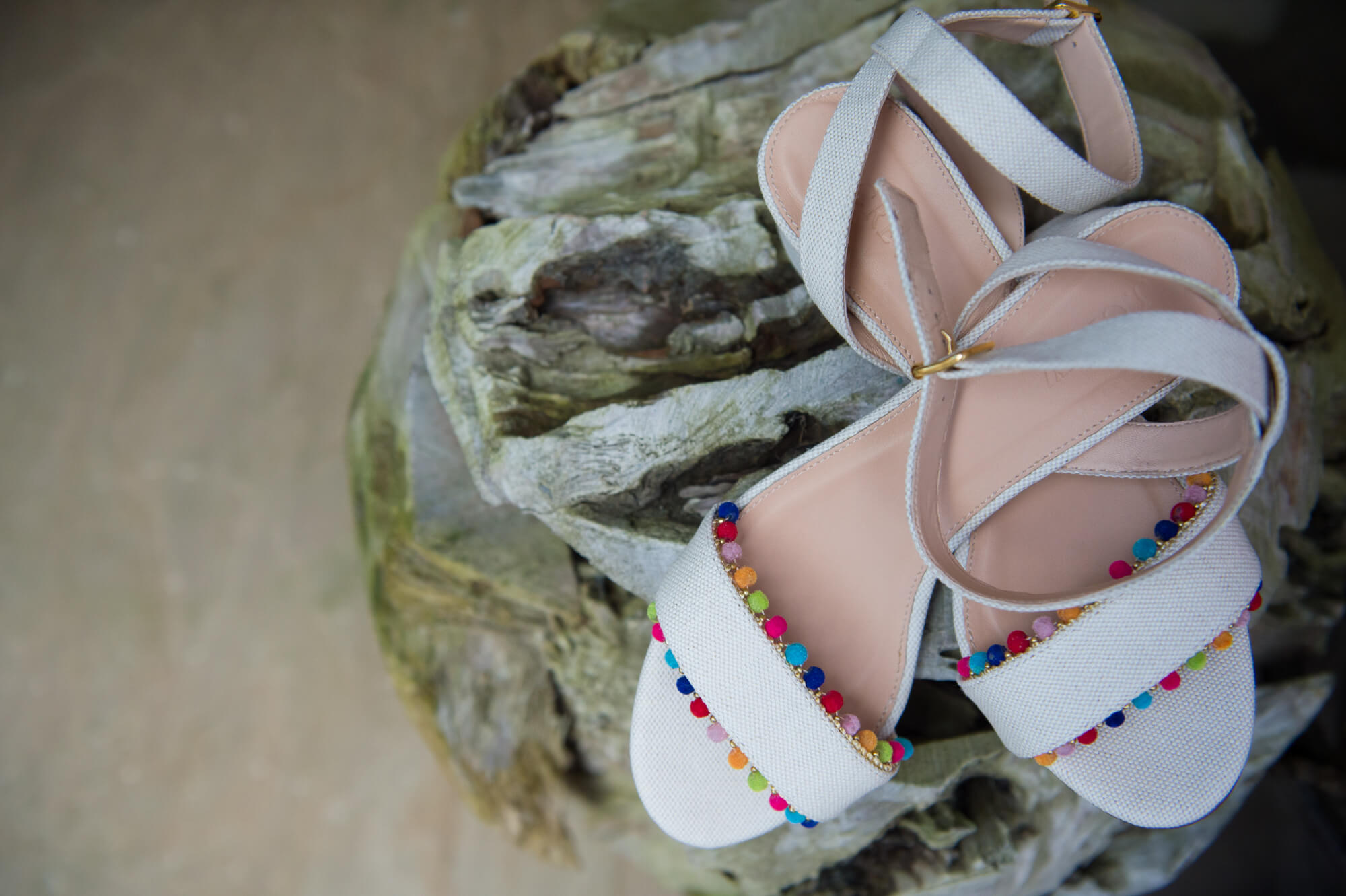 J Crew wedding shoes with pom poms sitting on a tree stump before the bride wears them